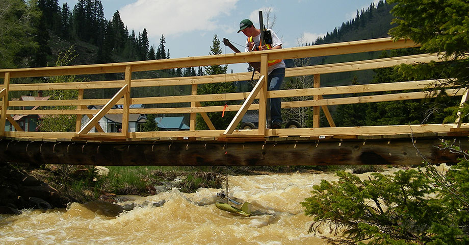 Scientist on Bridge Lowering Measuring Device Into Turbulent River.
