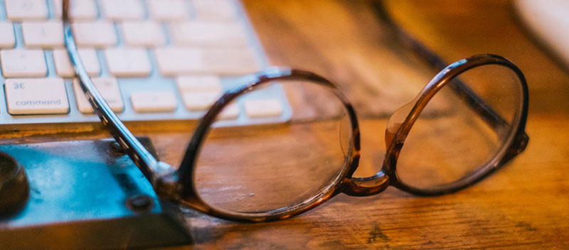 Glasses resting on a computer keyboard on a desk.
